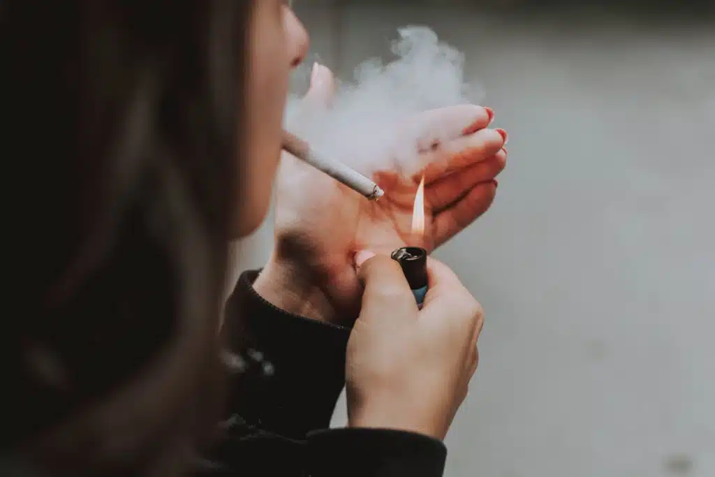 image of a female lighting a cigarette with a lighter.  Smoking, on average, increases life insurance rates by 3x.