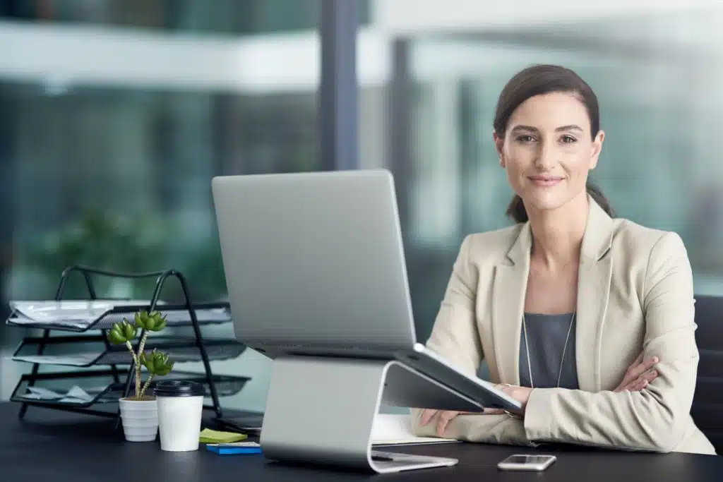 woman facing the camera while sitting at a desk with a laptop working in her job in finance
