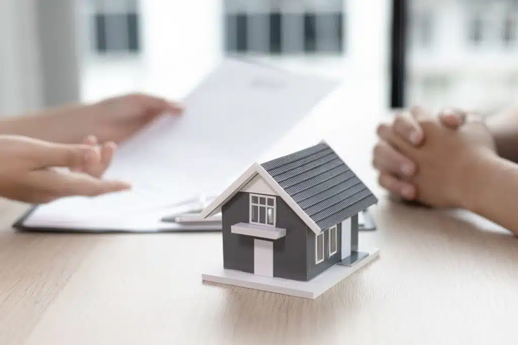 two people reviewing a contract at a desk with a model house in the foreground
