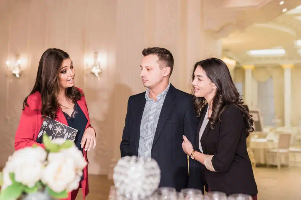 A female event planning speaking to a man and woman while holding a paper folder 