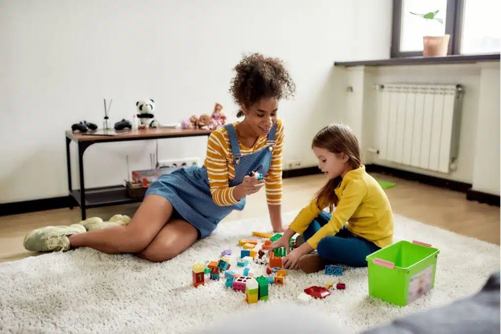 teenager playing lego with a young girl while sitting on the floor

